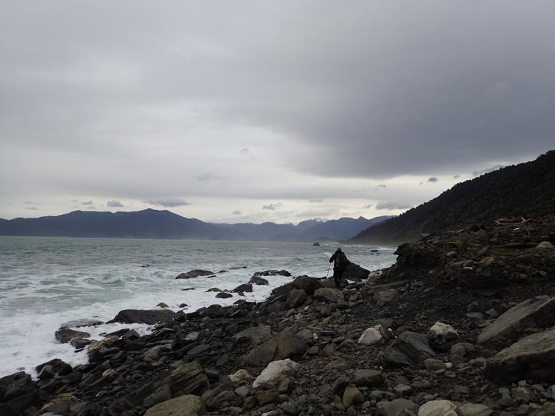 hiker walking along a rocky beach with ocean on the left