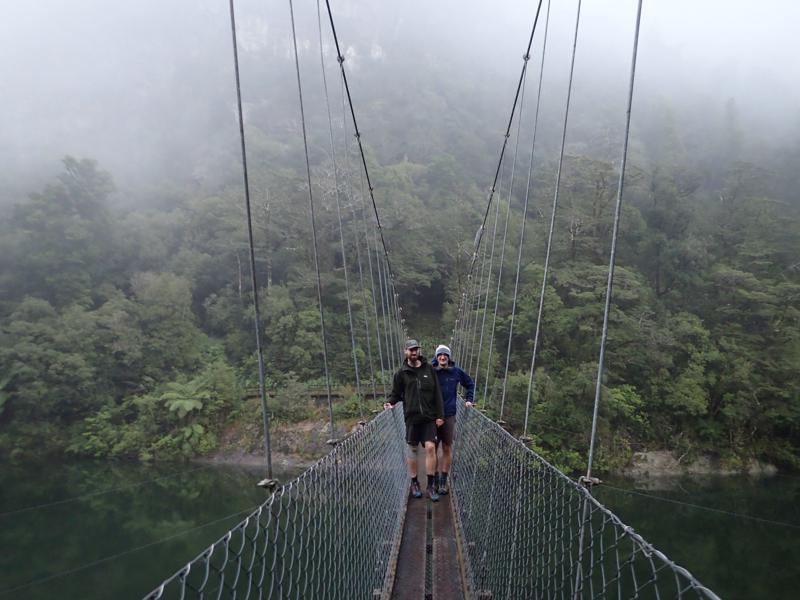 2 hikers standing on the middle of a narrow swing bridge