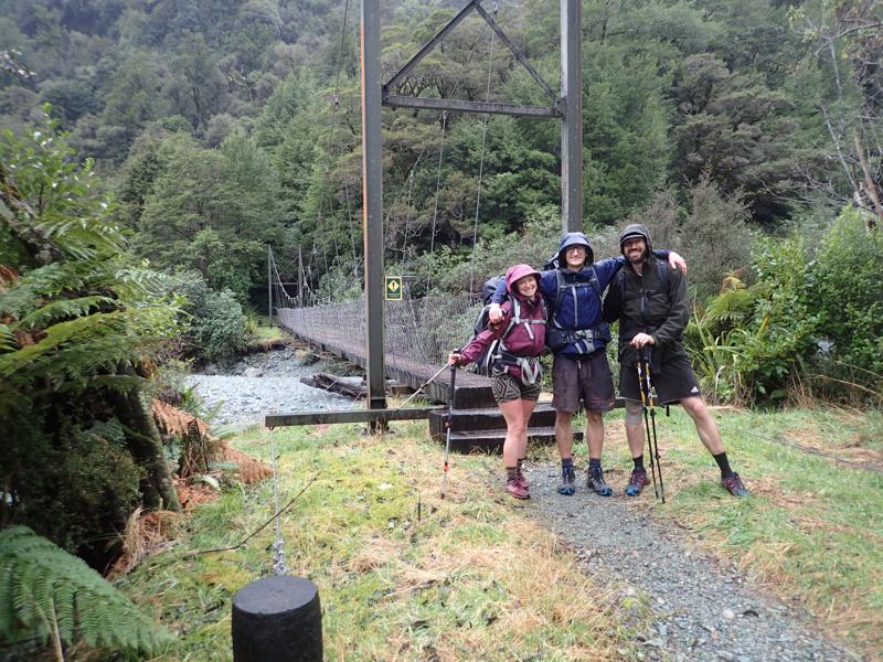 3 hikers hugging in front of a swing bridge