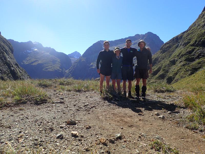 4 hikers on a mountain pass with blue sky and sunshine