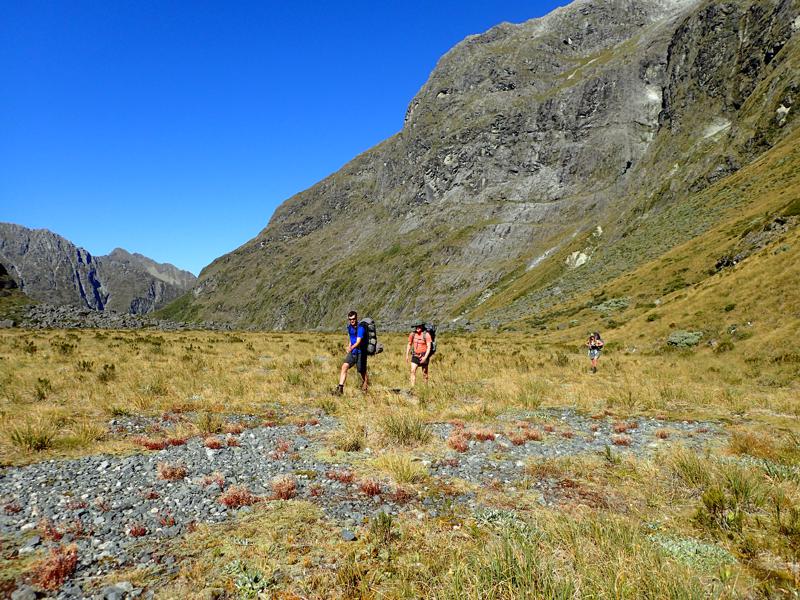 3 hikers crossing a flat basin with mountains behind