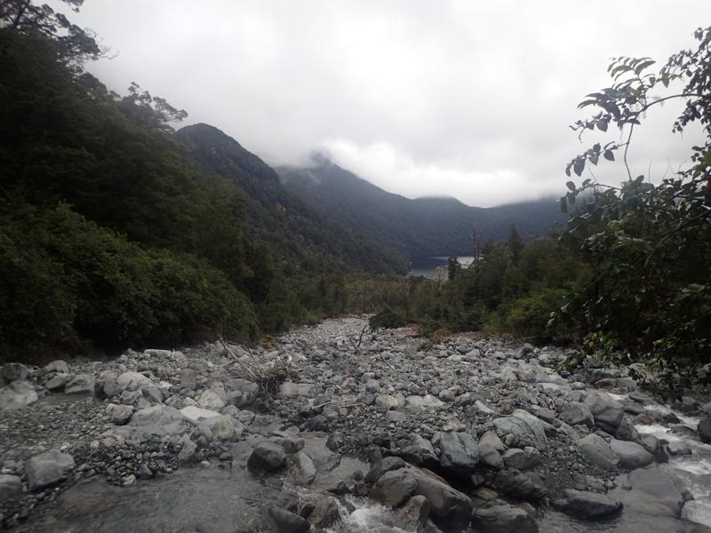 looking down a wide rocky river to a lake below with trees on either side