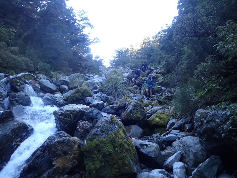 3 hikers scrambling down rocks alongside a steep creek