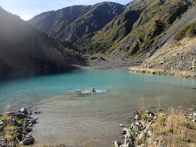 A hiker swimming in a small milky blue lake