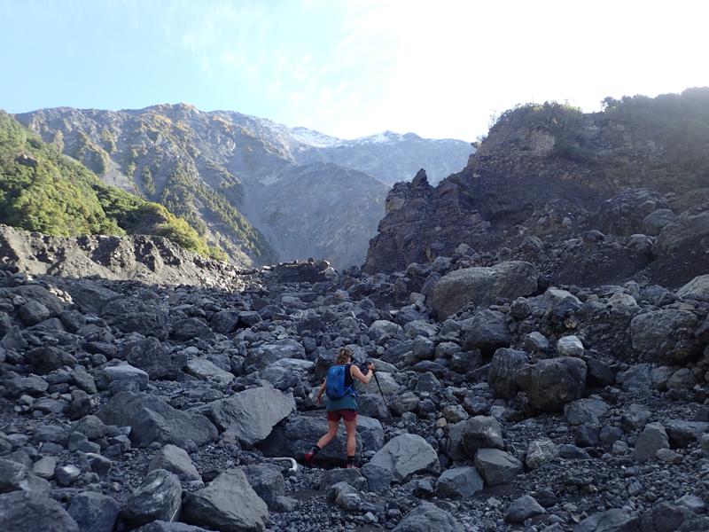 A hiker scrambling up and around rocks in a river valley