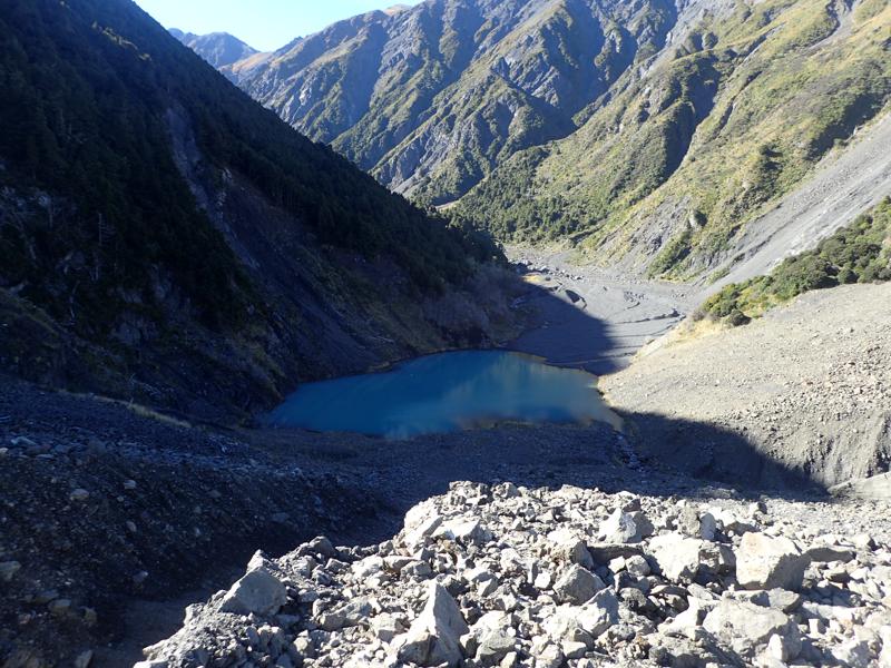 small lake at the base of rock wall, valley bending away around a corner