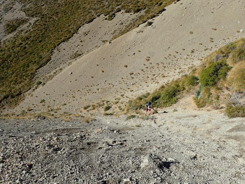 a hiker scrambling up steep loose gravel in the sunshine