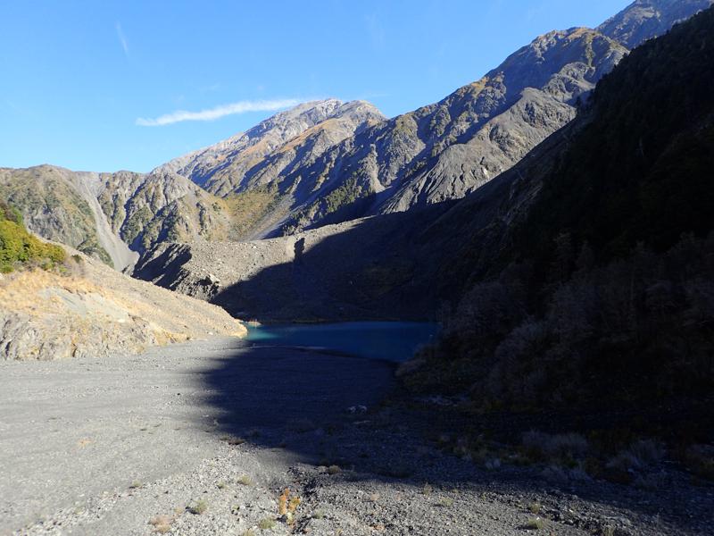 mountain valley with small lake in front of a large scree and rock wall