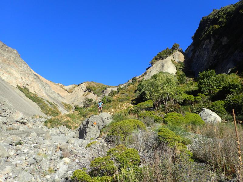 a hiker standing on rock in a narrowing and climbing valley, with blue sky behind