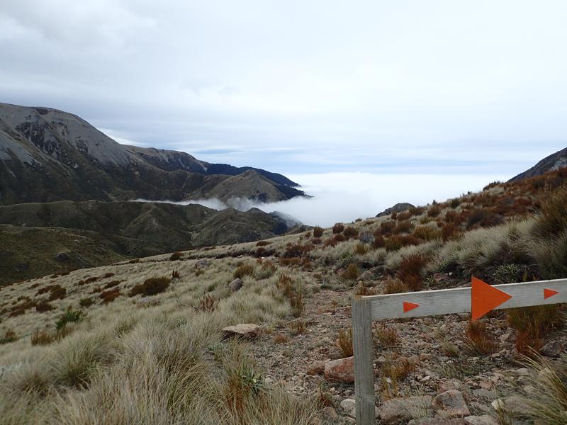 a track leading down into cloud with mountains beyond