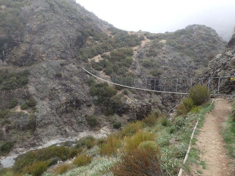 hiker crossing a swing bridge over a narrow gorge