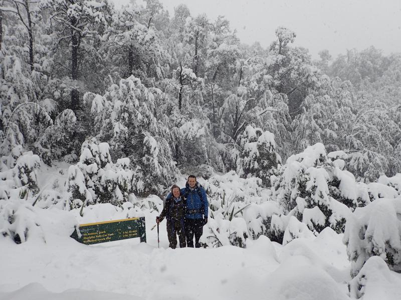 2 hikers standing in a snowy landscape beside a sign