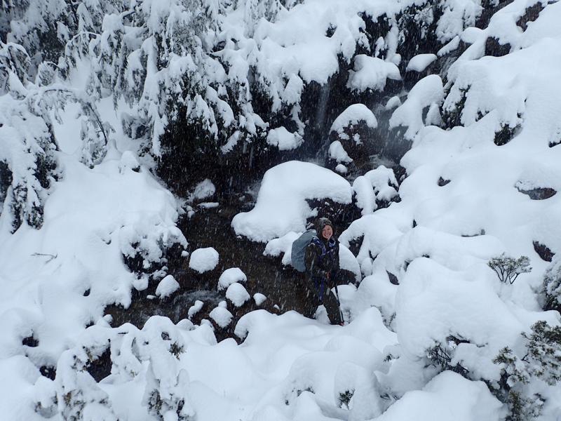 a hiker crossing a snowy creek