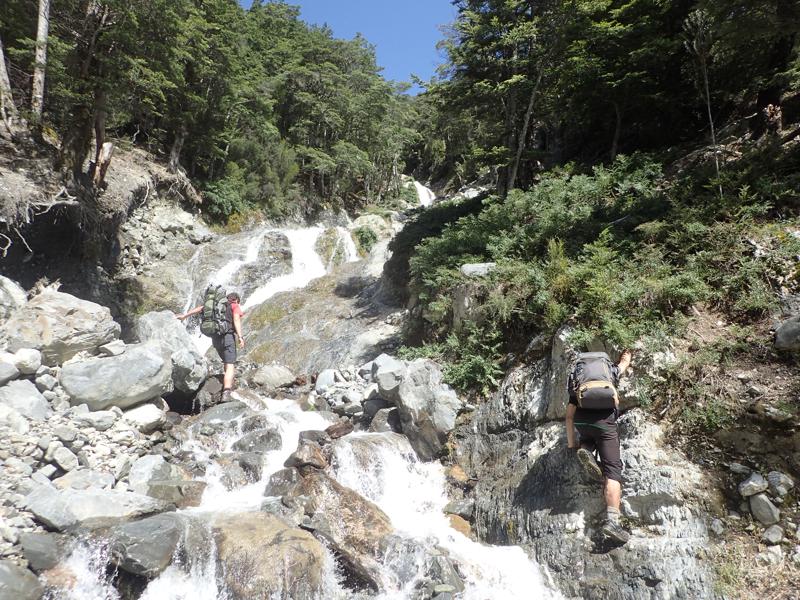 2 hikers climbing steeply up a small creek