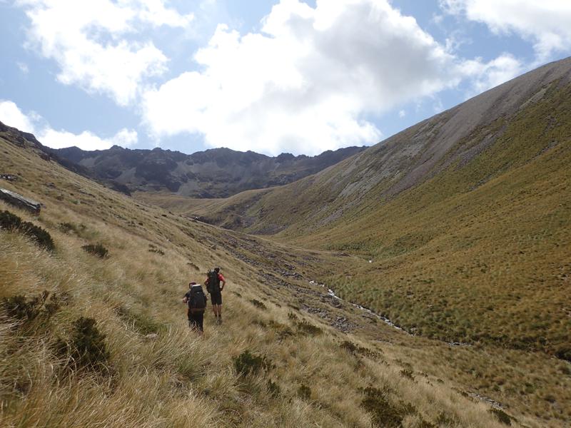 2 hikers walking up a grassy valley beside a stream