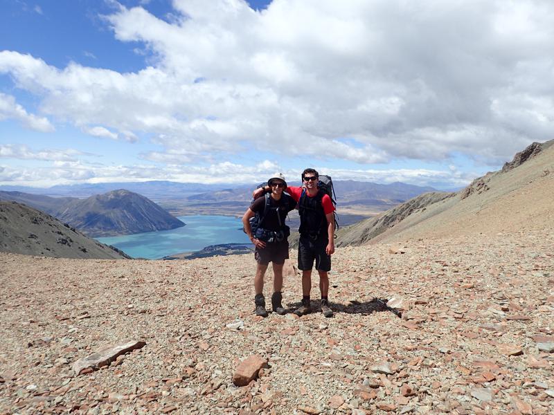 2 hikers on a rocky saddle with a big blue lake below