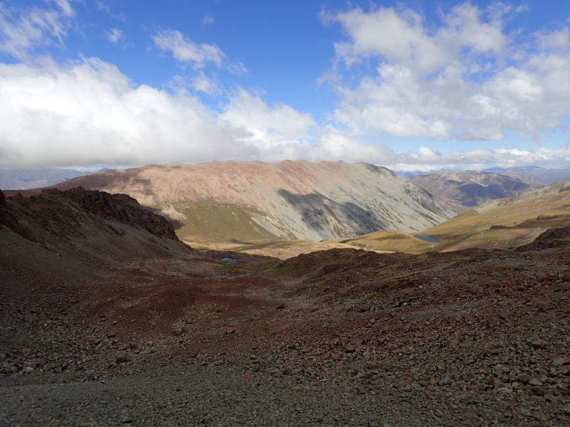 a rocky slope with rocky mountain beyond and 2 small lakes