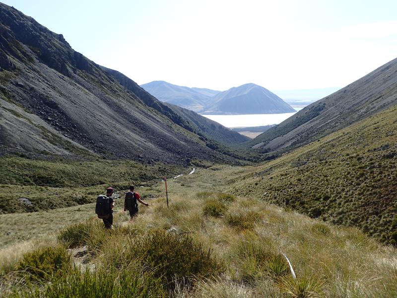 2 hikers descending into a valley with a lake beyond