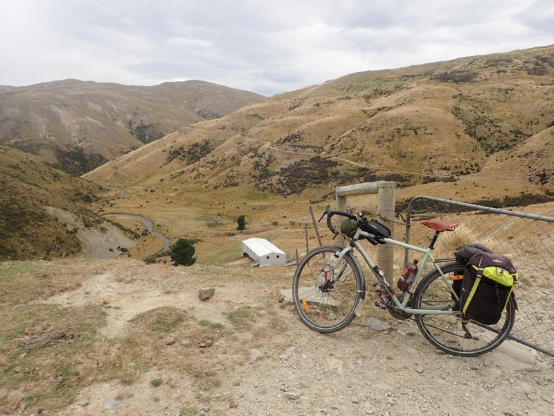 Bike resting against a gate with hills around and a winding track in the distance
