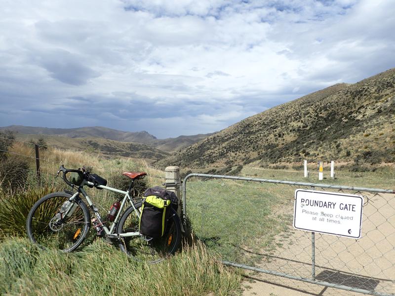 Bike resting against a fence with a gate beside and hills beyond