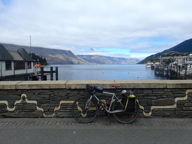 Bike against a wall with lake and buildings beyond and cloud cloaked mountains in the background