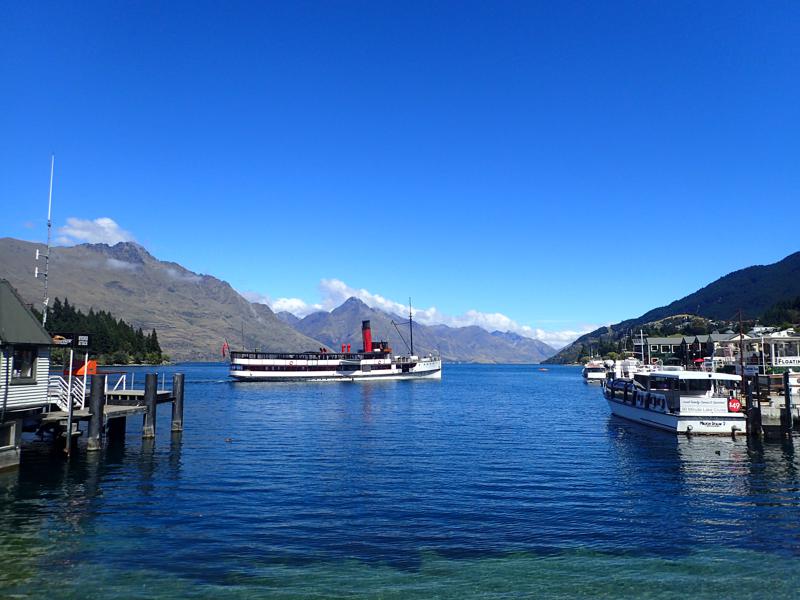 Steam ferry on a blue lake with sunny mountains behind