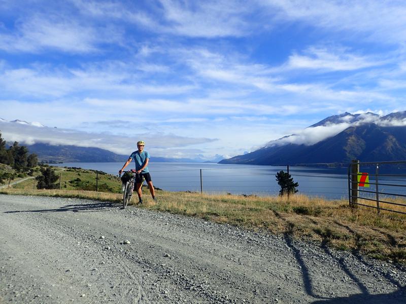 Cyclist with bike on gravel road with lake behind
