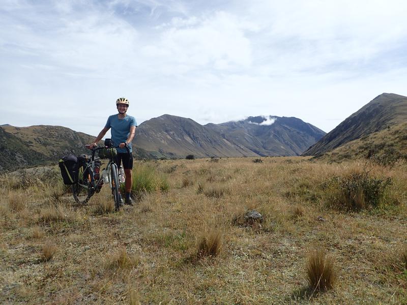 Cyclist with bike in tussock grass with mountains behind