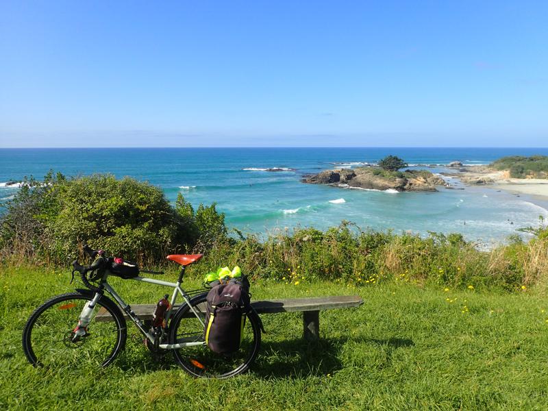 Bike leaning against a bench with a beach and coastline beyond