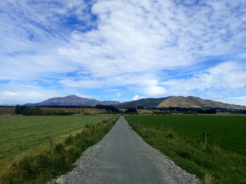 Straight gravel cycle path between two fields with blue skies