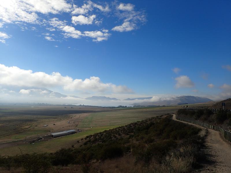 Cycle path descending into farmland with cloudy mountains beyond