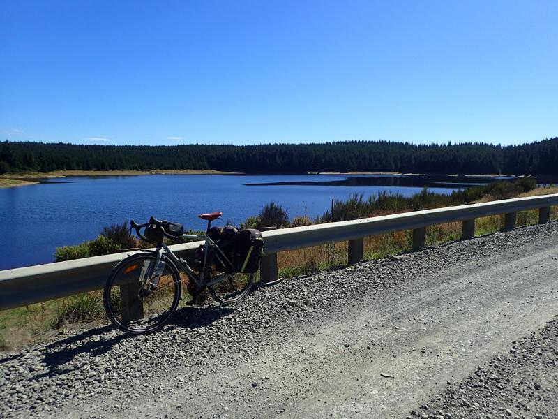 Bike on the side of a gravel road with a lake and foresty beyond