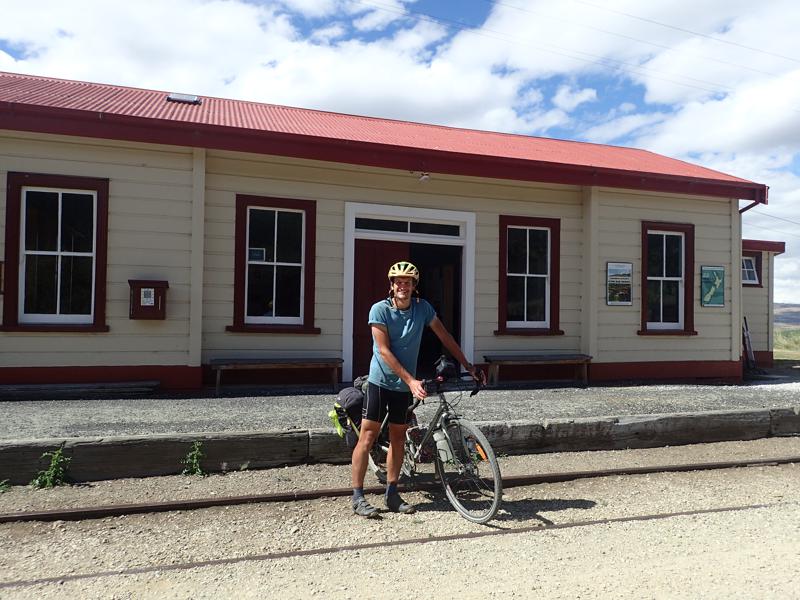 Cyclist holding bike in front of a cream and red coloured station building
