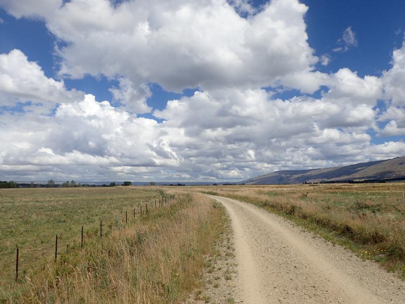 Gravel track stretching into distance across flat plains with cloudy skies