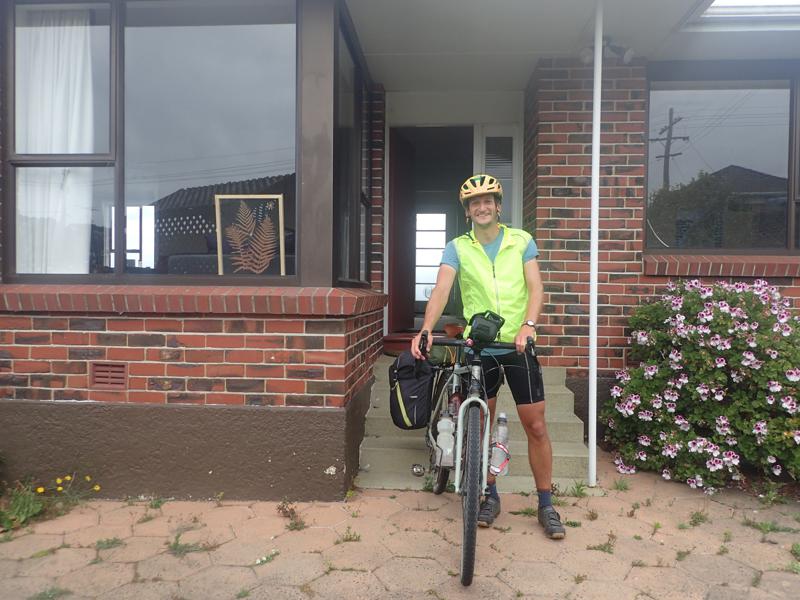 Smiling cyclist with bike outside house