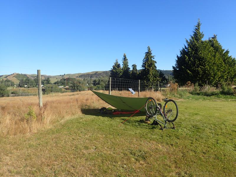 A tarpaulin stretched out tied to a fence and a upturned bicycle